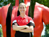 Natasha Dowie wearing a red and black AC Milan polo shirt standing in front of a statue at San Siro Stadium